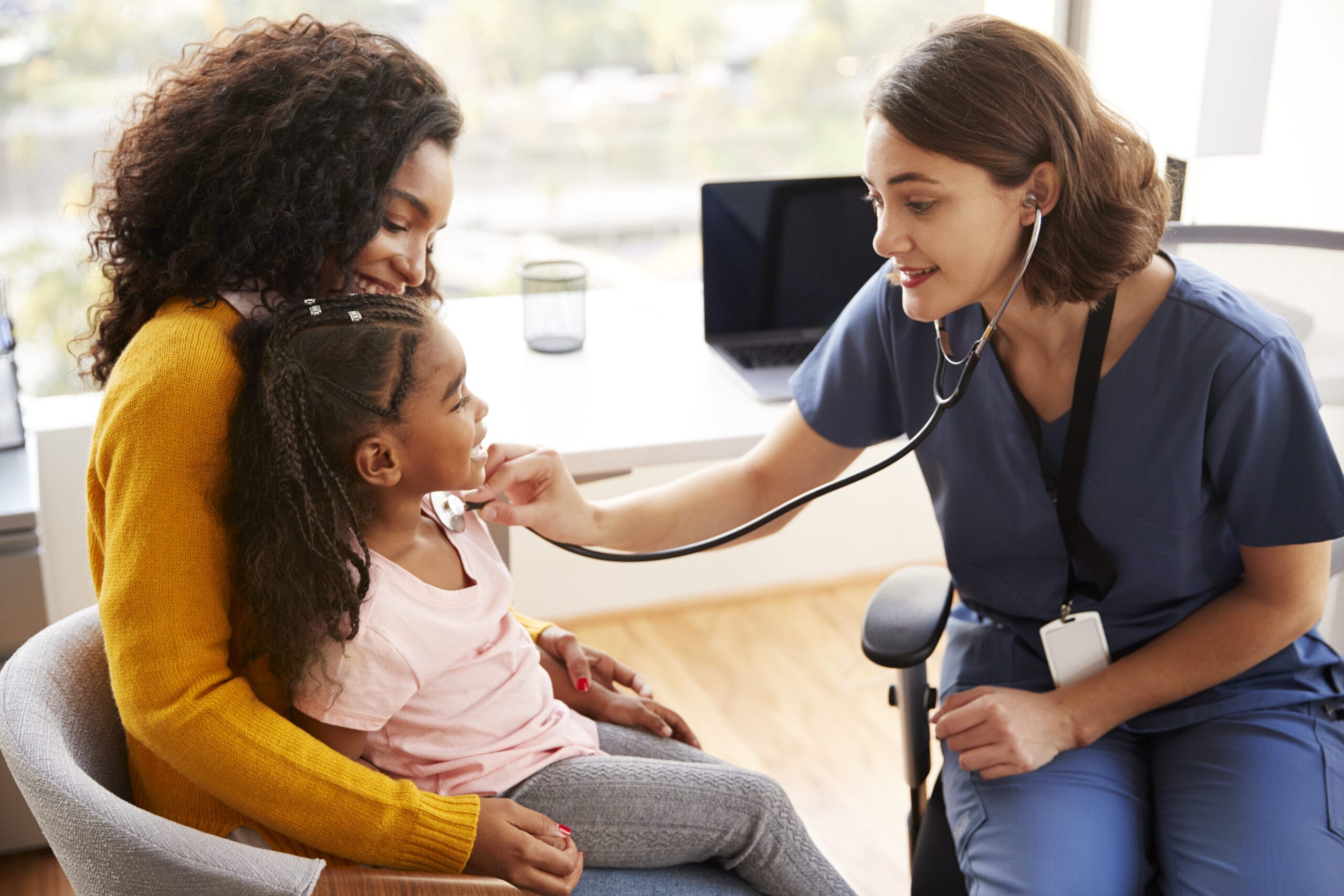 Nurse Wearing Scrubs Listening To Girls Chest With Stethoscope In Hospital Office