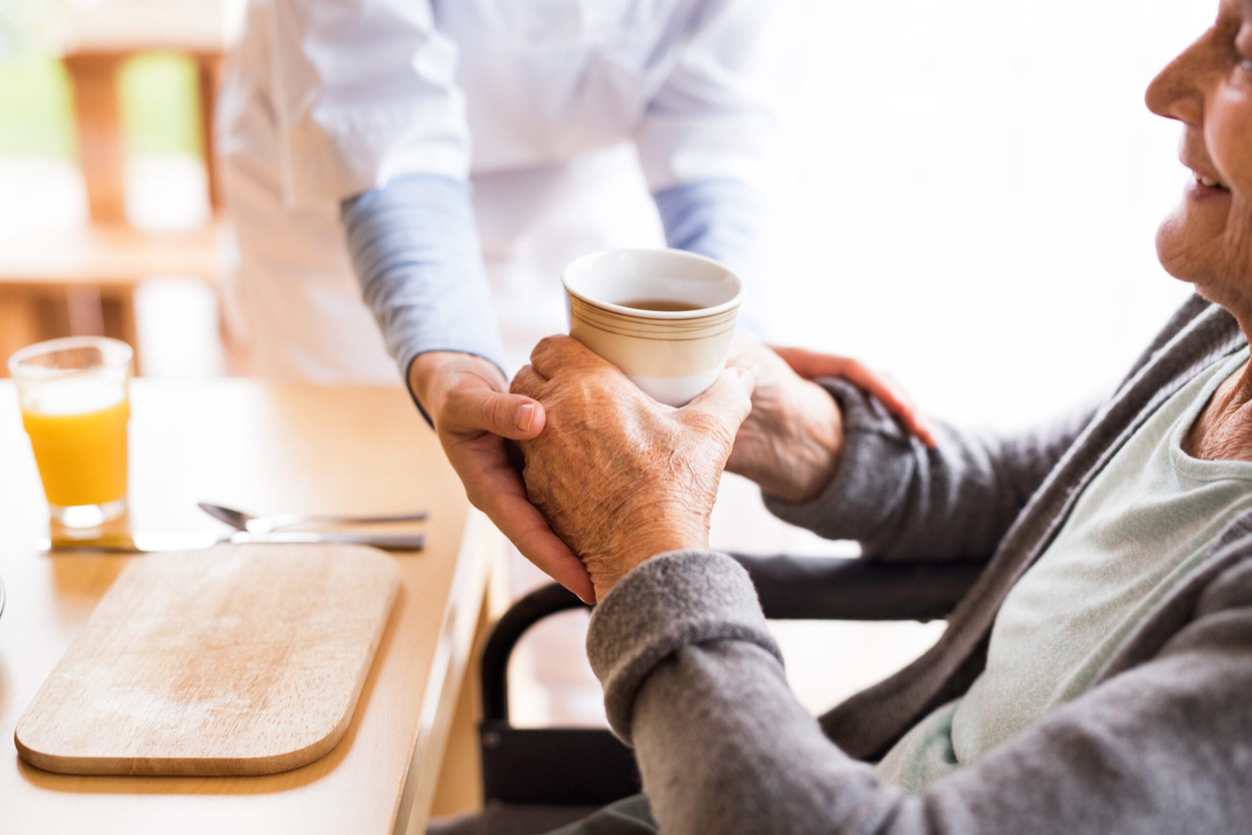 Caregiver assisting an elderly person with a cup of coffee